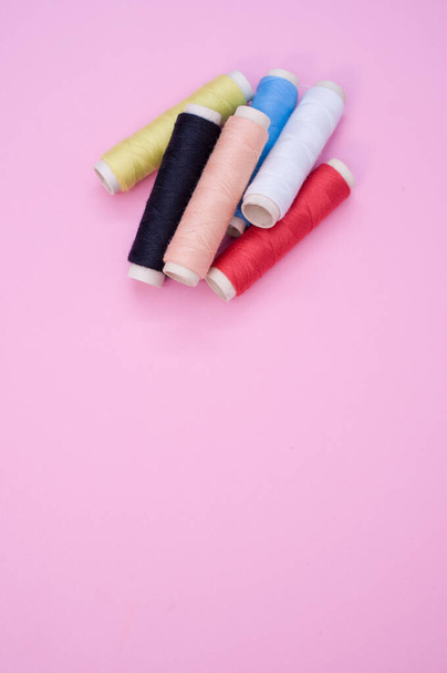 A closeup of the colorful sewing threads on the pink surface - space for text - 写真・画像