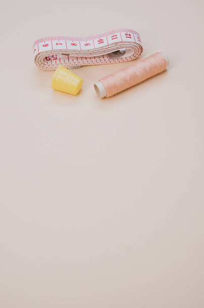A closeup of a pink  sewing thread with a thimble and a measuring tape on the brown surface - Fotografie, Obrázek
