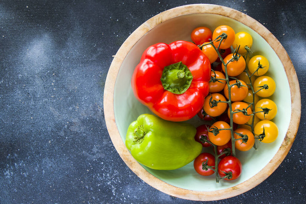 A top view of colorful bell peppers and cherry tomatoes in the bowl isolated on blue background - Photo, Image