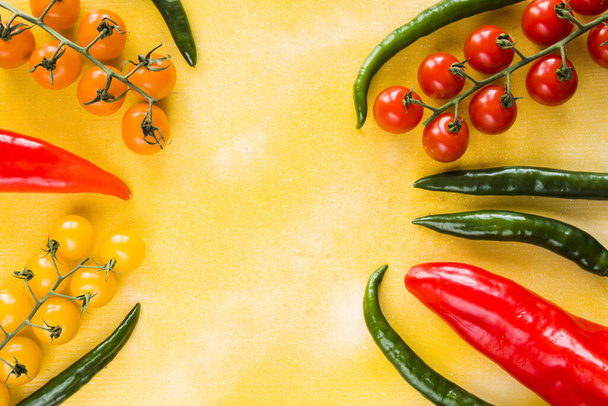 A red and green spicy pepper and colorful cherry tomatoes on a yellow background - Foto, Imagem
