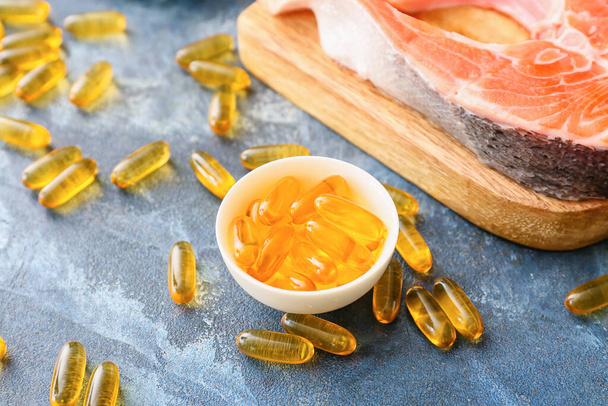 Filete de salmón crudo con píldoras de aceite de pescado sobre fondo de color - Foto, Imagen