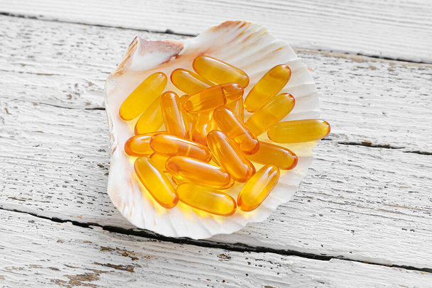 Sea shell with fish oil capsules on light wooden background - Photo, Image