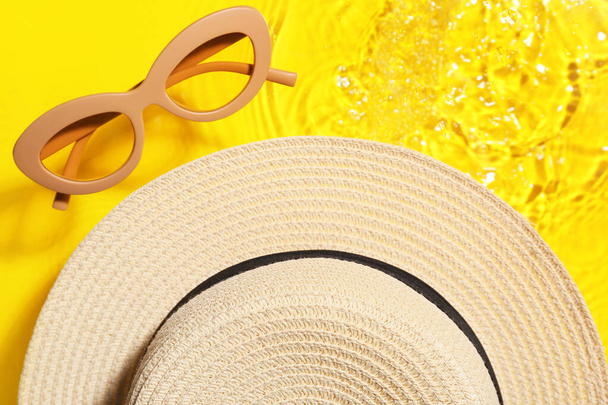 Стильная шляпа и солнцезащитные очки в воде на цветном фоне, крупный план - Фото, изображение