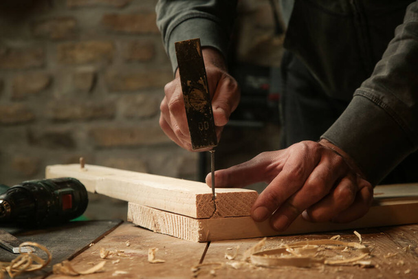 Плотник вбивает гвоздь в деревянную доску в мастерской. - Фото, изображение