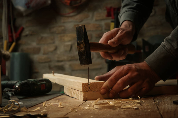 Timmerman hameren spijker in houten plank in werkplaats. - Foto, afbeelding