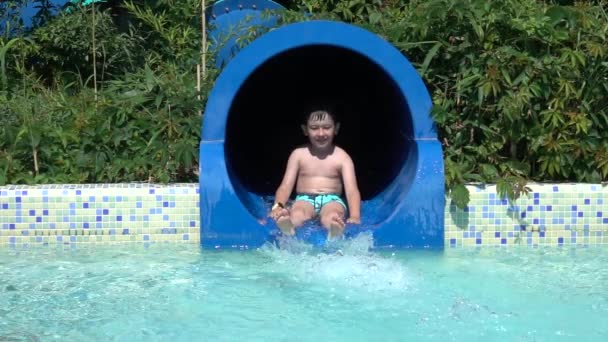 Çocuk yaz tatilinde su parkında kayıyor. Su kaydırağından kayan mutlu çocuk. Yavaş çekim 240 fps - Video, Çekim