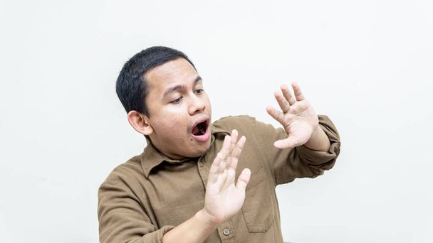 Горе и шокированное выражение лица молодого малайца в рубашке с поднятыми вверх обеими руками, смотрящего на пустое пространство на изолированном белом фоне. - Фото, изображение