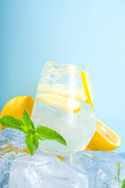 Geleneksel yaz soğuğu ferahlatıcı limonata, limon dilimleri, ezilmiş buzlar ve mavi arka planda buzlu kaideler.  - Fotoğraf, Görsel