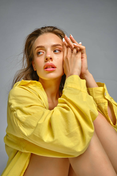 Pensive young woman in yellow shirt sitting on grey background - Foto, afbeelding