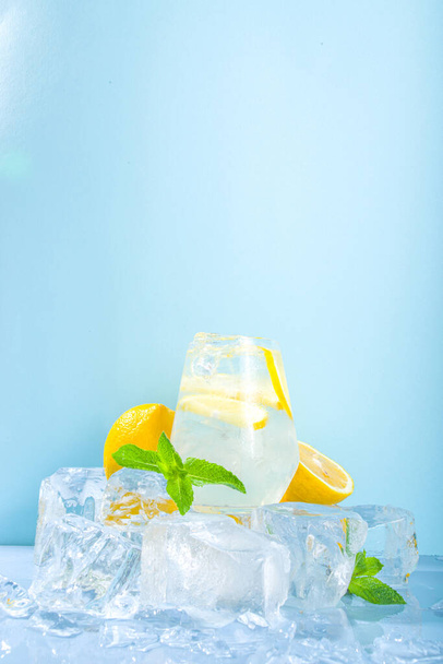 Hagyományos nyári hideg frissítő koktél limonádé, citromos szeletek és sok zúzott jég és jeges talapzat kék alapon  - Fotó, kép