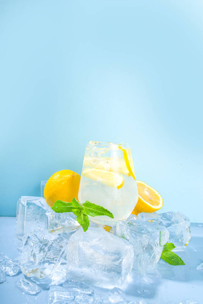 Citronnade rafraîchissante froide traditionnelle d'été, avec des tranches de citron et beaucoup de glace concassée et des piédestaux glacés sur fond bleu  - Photo, image