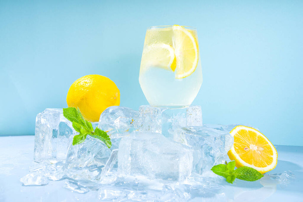 Hagyományos nyári hideg frissítő koktél limonádé, citromos szeletek és sok zúzott jég és jeges talapzat kék alapon  - Fotó, kép