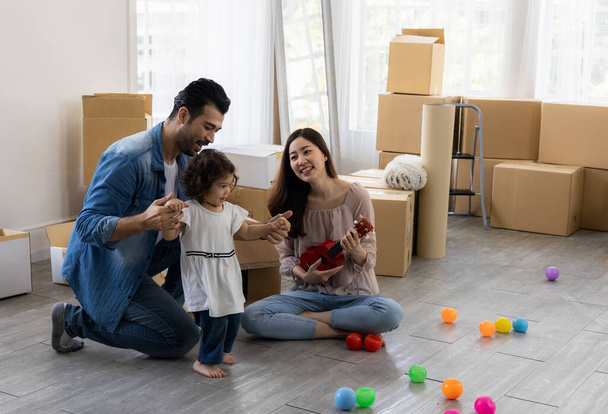 Rodiče a dcery si hrají s ukulele sedí na podlaze v obývacím pokoji doma. Rodina se právě přestěhovala do nového domu. Happy moment multi-etnický táta maminka a dítě. - Fotografie, Obrázek