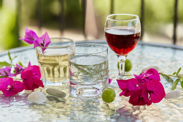 Sommer hausgemachte Cocktails und ein Glas Rotwein und rosa Blüten von Bougainvillea Dekorationen mit Kieselsteinen. Sommer Tapete aus nächster Nähe - Foto, Bild