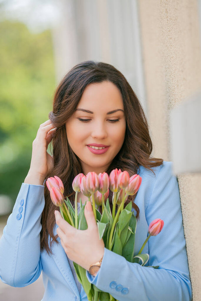 Retrato de uma bela jovem mulher em um terno azul com um buquê de tulipas. - Foto, Imagem