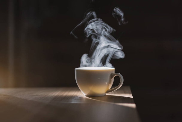 Hot water in white coffee cup on wooden table with smoke and nature light on black background - Foto, Bild