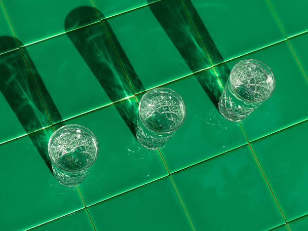 Verfrissende zomer drankjes in kristallen glazen op groene bar tegel achtergrond reflectie harde schaduw. Koude gin wodka cocktail voor warme zomerdag. Niet-alcoholische frisdrank helder water munt tonic. Feestdagen - Foto, afbeelding