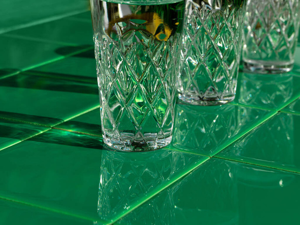 Refreshing summer drinks in crystal glasses on green bar tile background reflection harsh shadow. Cold gin vodka cocktail for hot summer day. Non alcoholic soda clear water mint tonic. Party vacation - Photo, Image