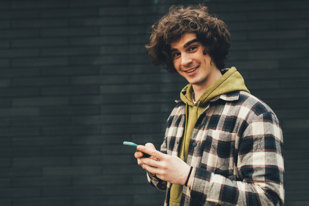 Χαμογελαστή άνθρωπος με κινητό τηλέφωνο στέκεται έξω  - Φωτογραφία, εικόνα