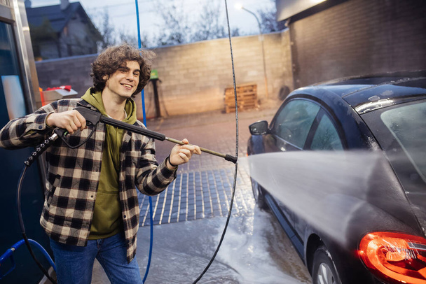 Веселый человек с моечной машиной давление очистки авто на самообслуживание мытье вечером  - Фото, изображение