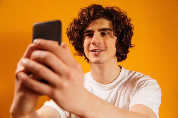 Uśmiechnięty mężczyzna korzystający ze smartfona na niewyraźnym pierwszym planie na pomarańczowym tle - Zdjęcie, obraz