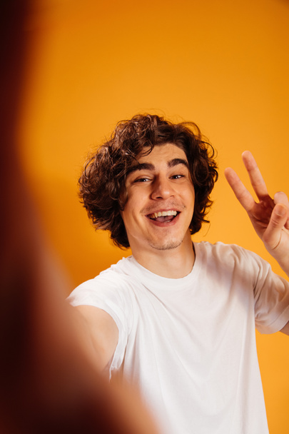 Happy man in white t-shirt showing peace sign on orange background - Photo, Image