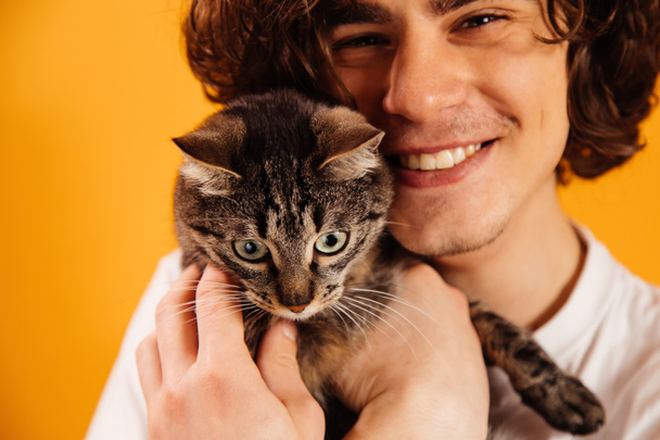 Γάτα στα χέρια του θολή άνθρωπος χαμογελά απομονωμένη σε πορτοκαλί  - Φωτογραφία, εικόνα