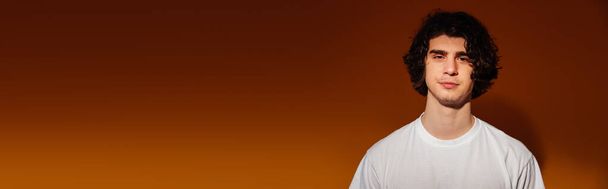 Man in white t-shirt looking at camera on brown background, banner  - Foto, Bild