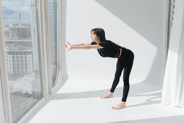 armenian woman in black sportswear practicing yoga in forward bend pose in sunshine - Photo, Image