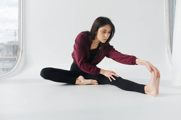 брюнетка вірменка практикує сидячу вперед вигин позу на білій підлозі
 - Фото, зображення
