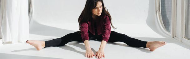 barefoot armenian woman sitting in wide-legged forward bend pose on white floor, banner  - Photo, Image