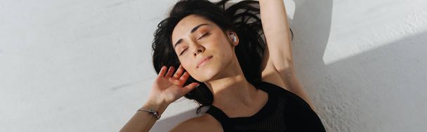 top view of brunette armenian woman with closed eyes lying on white with shadows, banner - Fotó, kép
