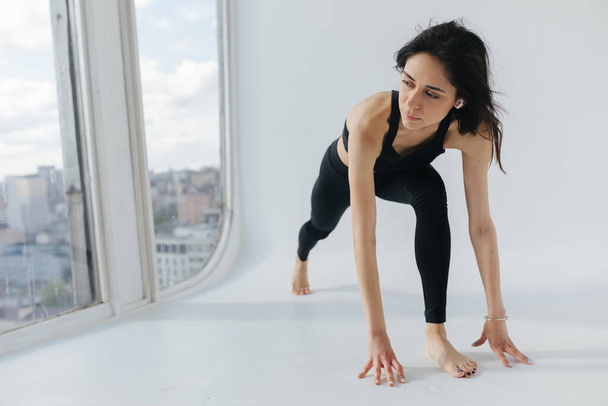 jeune femme arménienne en vêtements de sport noirs pratiquant le yoga dans la pose de fente - Photo, image