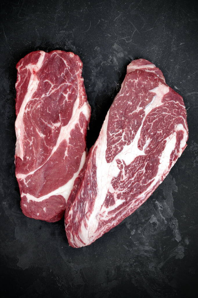 Raw Steaks. Sirloin Beef Steaks, Overhead View. Many Raw Striploin Steaks from Marbled Beef on Black Background. Group of Black Angus Beefsteaks. Raw Sirloin Cuts. Uncooked Prime Beef Steaks. - Photo, Image