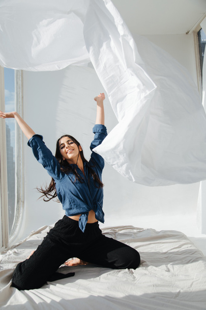 cheerful armenian woman throwing up white sheet in bedroom - Photo, Image