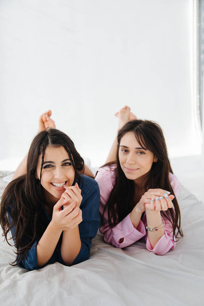 young and happy armenian women smiling at camera while lying on white bedding - Фото, зображення