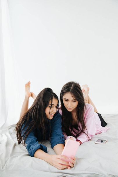 young, pretty armenian friends looking at smartphone while lying in bedroom - Photo, Image