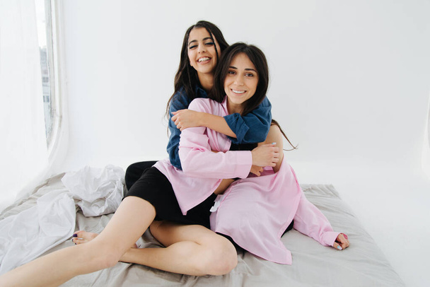 Paar junger und fröhlicher armenischer Frauen, die in die Kamera schauen, während sie sich im Schlafzimmer umarmen - Foto, Bild