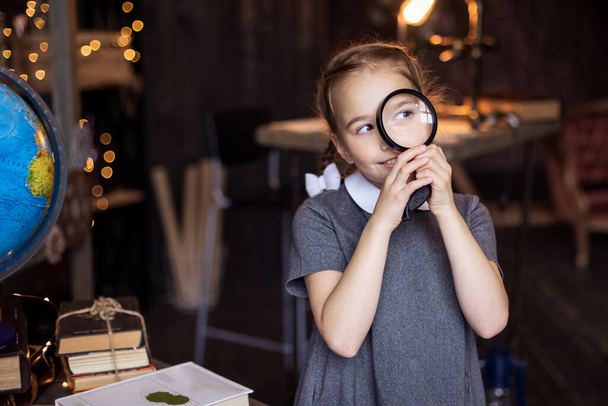 girl looks through a magnifying glass at nature lesson. Young biologist researcher. Detective game. School education knowledge. Primary School. A curious portrait of a schoolgirl. Classroom. Explorer - Fotografie, Obrázek