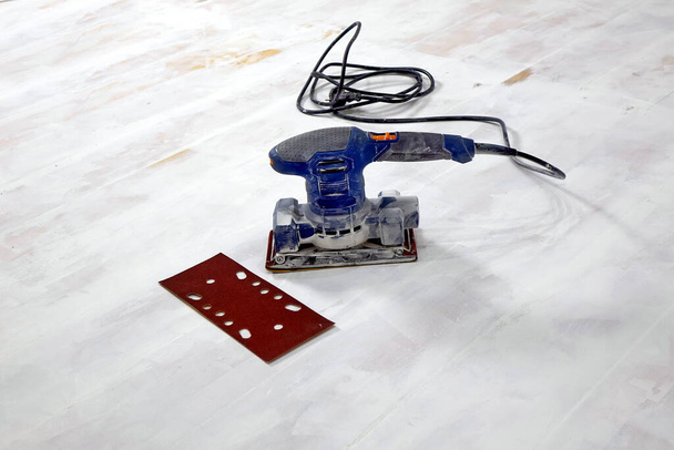 Elektrische schuurmachine op de houten vloer met schuurpapier - Foto, afbeelding
