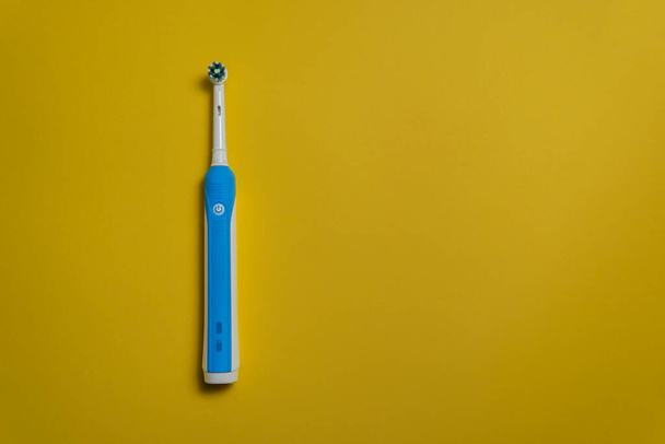 Moderne elektrische tandenborstel op gele achtergrond. Bovenaanzicht. Tandverzorging. Minimalisme. - Foto, afbeelding