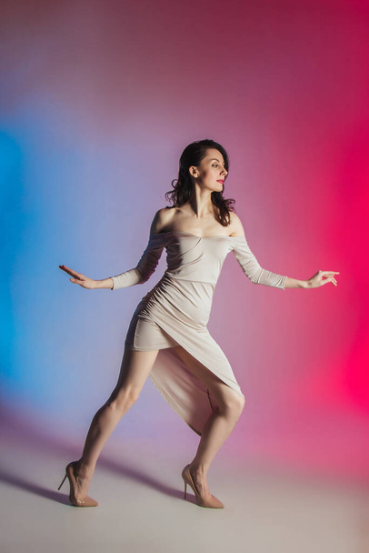 Farbigen Hintergrund, Neonlichter, Studioaufnahmen. Modeporträt einer jungen eleganten brünetten Frau in einem schönen Kleid - Foto, Bild