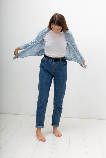 young caucasian pretty girl with long hair in shirt, blue jeans poses at studio - Foto, immagini