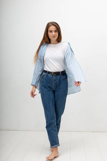 young caucasian pretty girl with long hair in shirt, blue jeans poses at studio - Zdjęcie, obraz