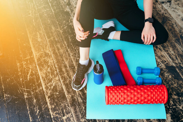  fitness instructor is sitting on the floor. sports equipment, dumbbells, elastic band, fascia roll lie on the yoga mat. - Fotografie, Obrázek