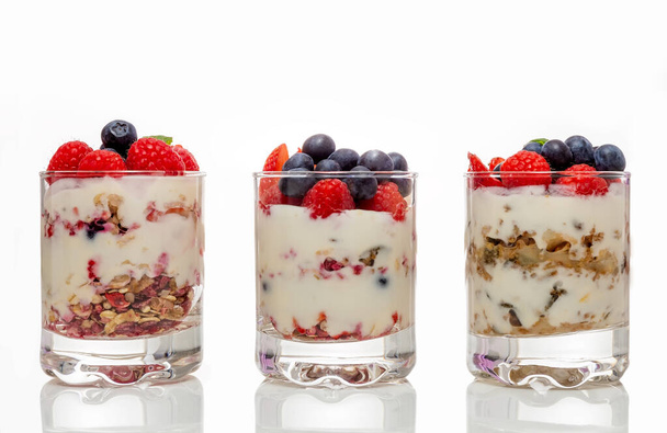 Muesli met yoghurt en bessen in een glas Op een witte achtergrond. Bereidingsproces voor dessert. Fitness eten. Begrepen, ruimte. Hoge kwaliteit foto - Foto, afbeelding