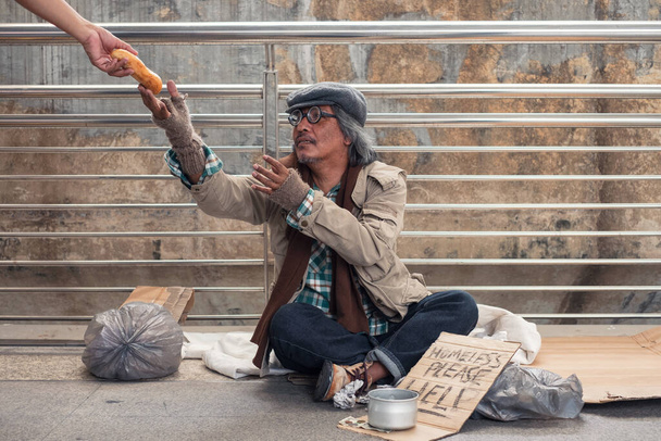 Ηλικιωμένοι άστεγοι ζητιάνοι απλώνονται για να πάρουν ψωμί στο χέρι δότη στη γέφυρα του διαδρόμου - Φωτογραφία, εικόνα