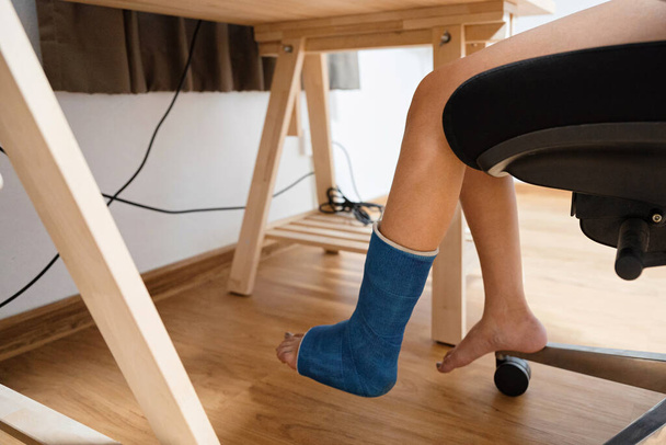 Mujer lesionada de pierna rota en yeso trabajando en escritorio de madera - Foto, Imagen