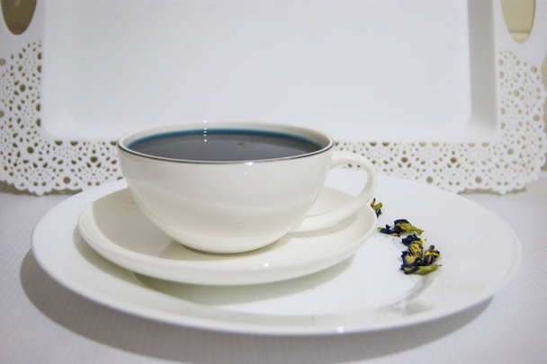 Ruh hali rengi mavi. Beyaz bir fincan çay bardağındaki mavi çay. Beyaz bir fincan tabağı ve beyaz bir tepside duruyor. Yararlı içkiler, iyileştirici özellikler. Beden eğitimi. Çay partisi.. - Fotoğraf, Görsel