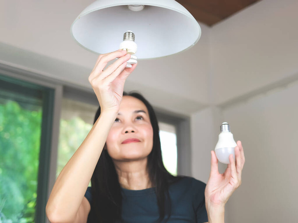 Femme asiatique changer ampoule, de spirale ampoule à ampoule LED. Focus sélectif sur le dessus. - Photo, image